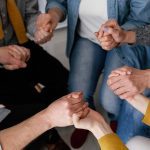 Grupo de pessoas de mãos dadas em círculo, simbolizando apoio e união.