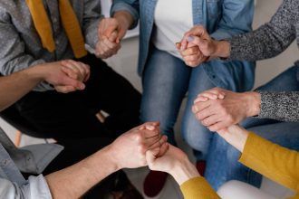 Grupo de pessoas de mãos dadas em círculo, simbolizando apoio e união.