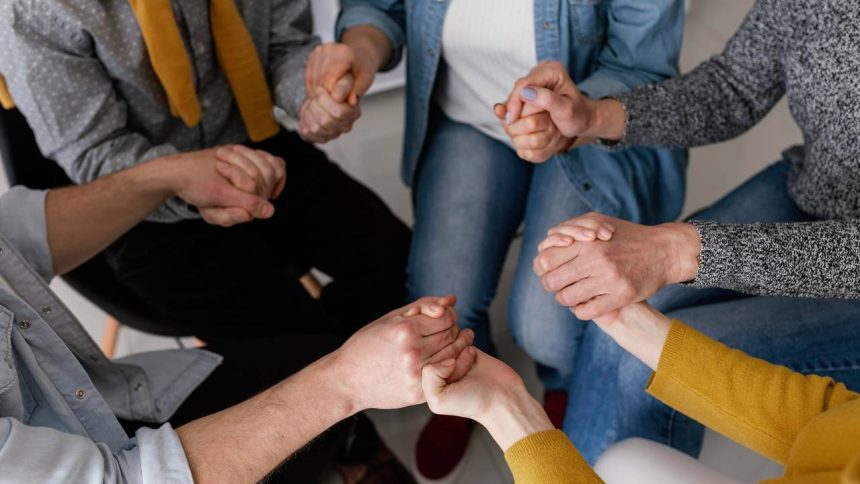 Grupo de pessoas de mãos dadas em círculo, simbolizando apoio e união.