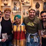 Grupo de pessoas sorrindo com livros, em evento de oficinas gratuitas 'Aglomeração Literária' no Amazonas.