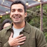 Gustavo Lins sorrindo com a mão no peito.