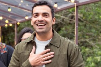 Gustavo Lins sorrindo com a mão no peito.