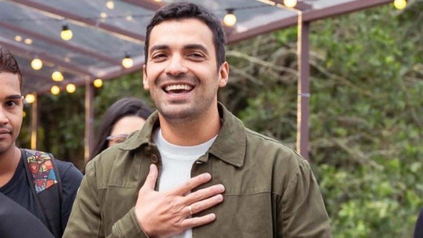 Gustavo Lins sorrindo com a mão no peito.