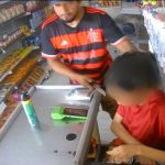 Homem armado com faca rende criança em comércio, registrado por câmera de segurança.