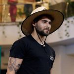 Homem com chapéu de palha e tatuagem no braço, possivelmente em um evento de moda.