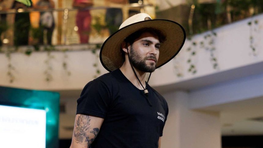 Homem com chapéu de palha e tatuagem no braço, possivelmente em um evento de moda.