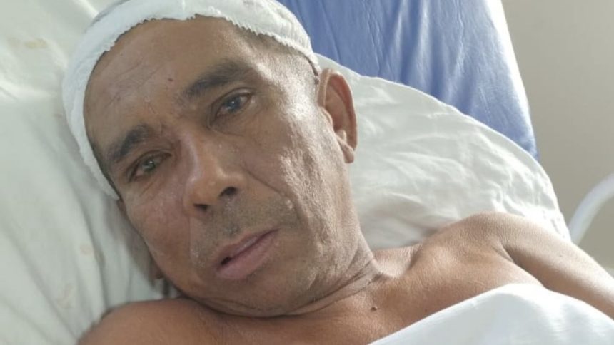 Homem em leito hospitalar com curativo na cabeça, possivelmente em busca de familiares.