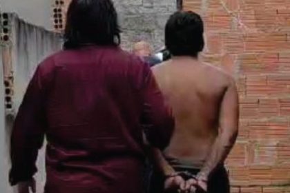Homem preso com as mãos algemadas, acompanhado por policial