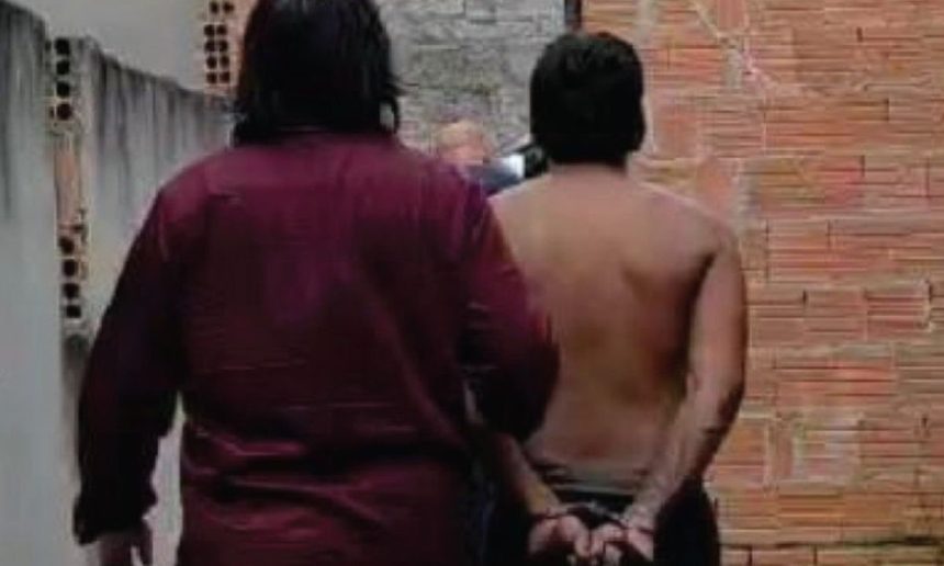 Homem preso com as mãos algemadas, acompanhado por policial