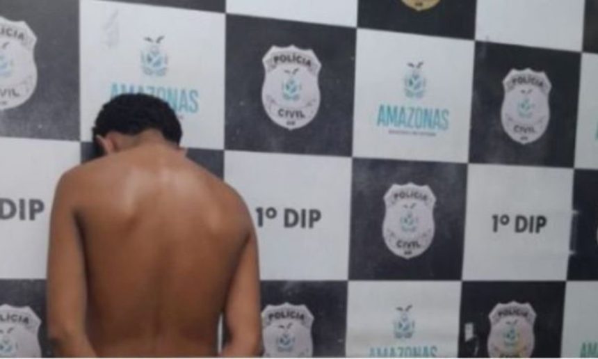 Homem preso em operação policial, encostado em uma parede com o brasão da polícia.