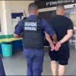 Homem preso por guardas municipais em frente a uma porta de vidro.