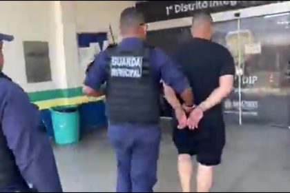 Homem preso por guardas municipais em frente a uma porta de vidro.
