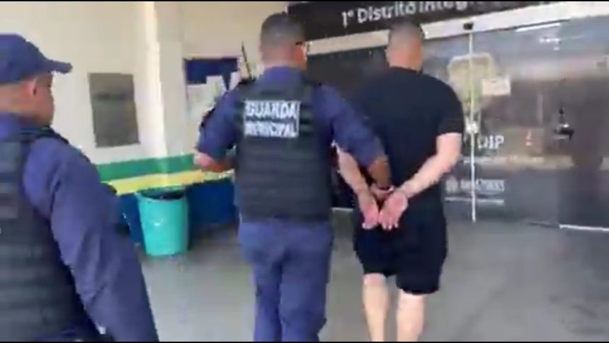 Homem preso por guardas municipais em frente a uma porta de vidro.