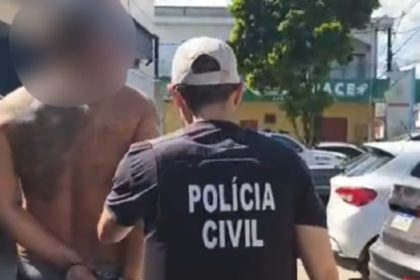 Homem preso sendo conduzido por policial civil. O homem está sem camisa, com tatuagens e algemado.