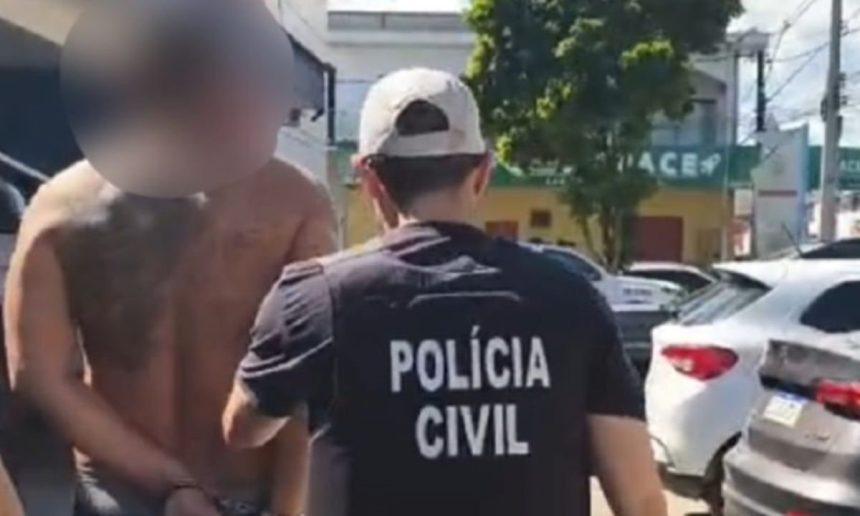Homem preso sendo conduzido por policial civil. O homem está sem camisa, com tatuagens e algemado.