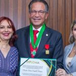 Homem recebe diploma ladeado por duas mulheres, celebrando sua dedicação à Justiça.