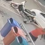 Homem se aproxima de carro e moto em estacionamento, possivelmente envolvido em incidente.