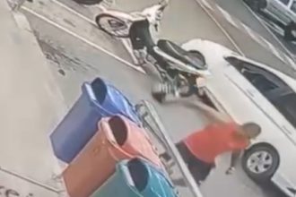 Homem se aproxima de carro e moto em estacionamento, possivelmente envolvido em incidente.