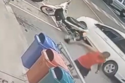 Homem se aproxima de carro e moto em estacionamento, possivelmente envolvido em incidente.