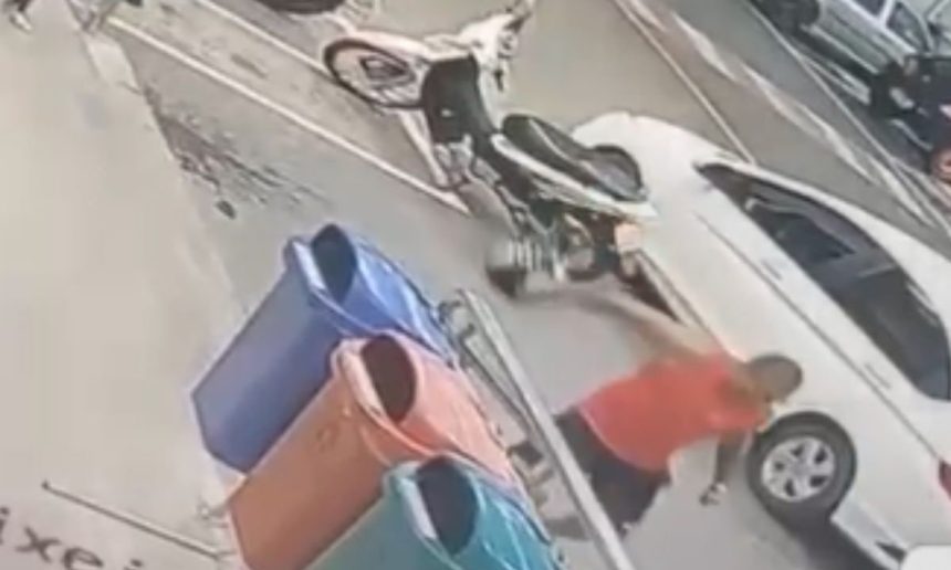 Homem se aproxima de carro e moto em estacionamento, possivelmente envolvido em incidente.