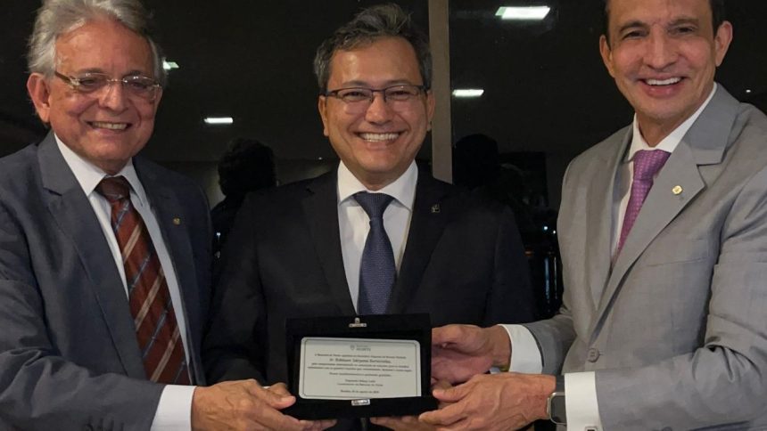 Homenagem a Dr. Edmison Jukiyama Barroso pela Receita Federal, com três homens sorrindo e segurando uma placa.