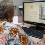 Idosa consultando cartilha de proteção contra fraudes financeiras para idosos em computador.