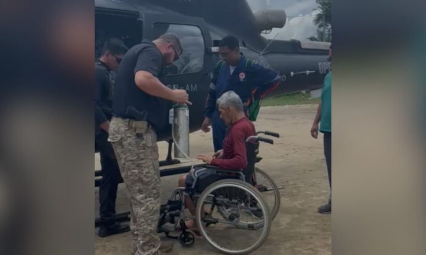 Idoso em cadeira de rodas sendo assistido por equipe de resgate perto de um helicóptero.