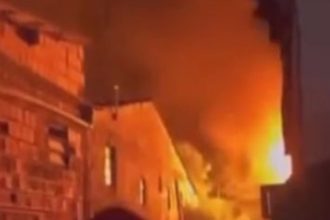 Incêndio em residência com chamas alaranjadas e fumaça densa.