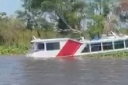 Lancha alagada em rio com parte submersa, com árvores ao fundo.