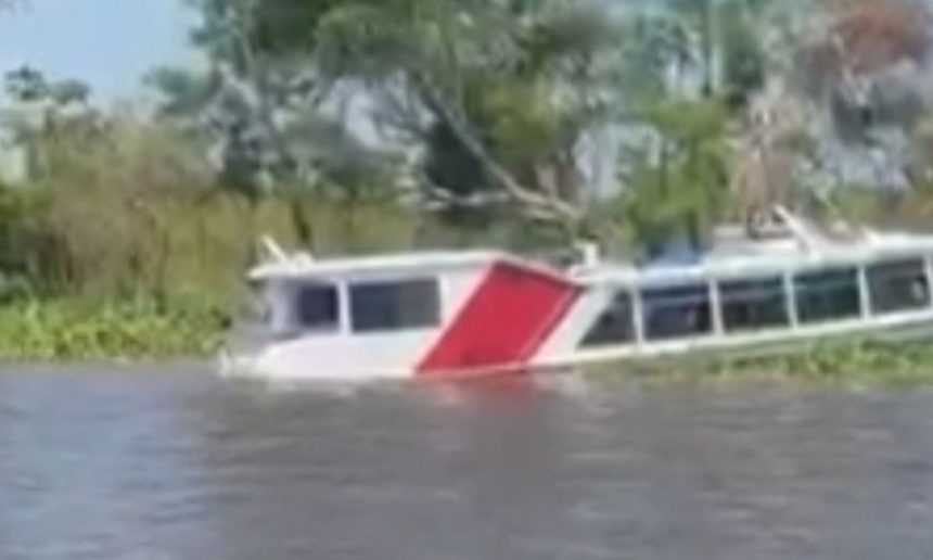 Lancha alagada em rio com parte submersa, com árvores ao fundo.