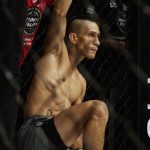 Lutador de MMA Arcanjo 'Anjo' em pose de concentração dentro do octógono, exibindo físico atlético e tatuagem.