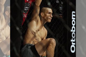 Lutador de MMA Arcanjo 'Anjo' em pose de concentração dentro do octógono, exibindo físico atlético e tatuagem.