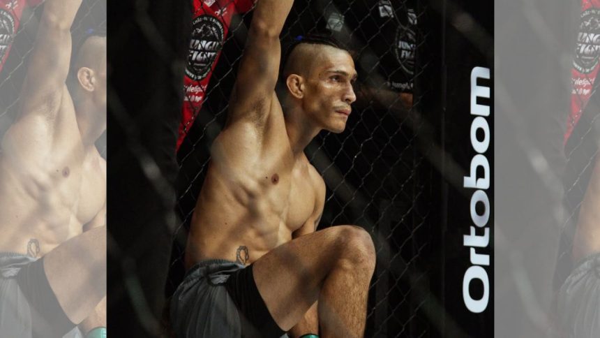 Lutador de MMA Arcanjo 'Anjo' em pose de concentração dentro do octógono, exibindo físico atlético e tatuagem.