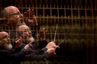 Maestro conduzindo orquestra, com efeito de múltiplas exposições, usando uma batuta e vestindo roupa preta.
