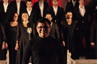 Maestro sorrindo com coral ao fundo.