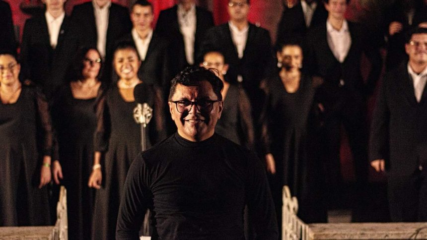 Maestro sorrindo com coral ao fundo.