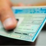 Mão segurando CNH (Carteira Nacional de Habilitação) azul e verde.