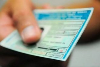 Mão segurando CNH (Carteira Nacional de Habilitação) azul e verde.