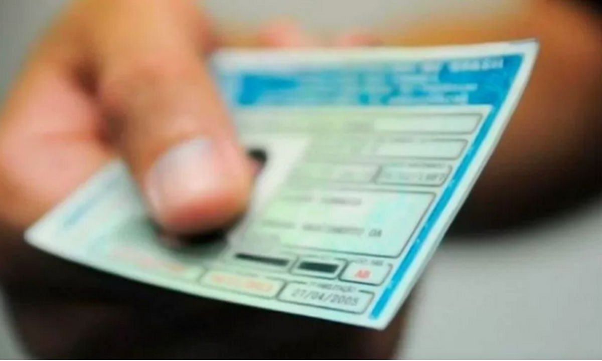 Mão segurando CNH (Carteira Nacional de Habilitação) azul e verde.