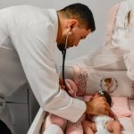 Médico examina recém-nascida em berço decorado em tons de rosa.