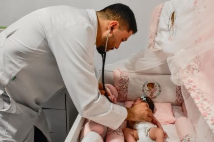 Médico examina recém-nascida em berço decorado em tons de rosa.