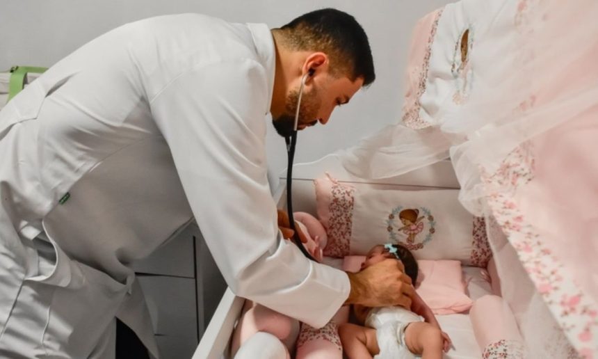 Médico examina recém-nascida em berço decorado em tons de rosa.