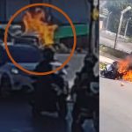 Motocicleta em chamas após acidente trágico, com bombeiros e carro nas proximidades.