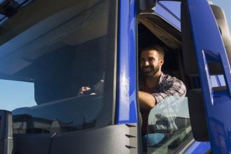Motorista sorrindo na cabine de um caminhão azul, concorrendo a prêmio do SEST SENAT.