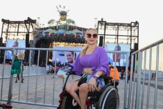 Mulher em cadeira de rodas segura ingresso para festival #SouManaus, com palco ao fundo.
