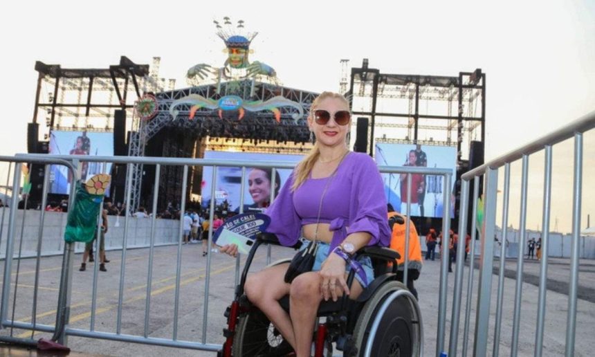 Mulher em cadeira de rodas segura ingresso para festival #SouManaus, com palco ao fundo.