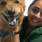 Mulher sorrindo abraçando um cachorro com sinais de câncer.