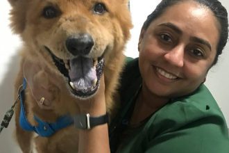 Mulher sorrindo abraçando um cachorro com sinais de câncer.