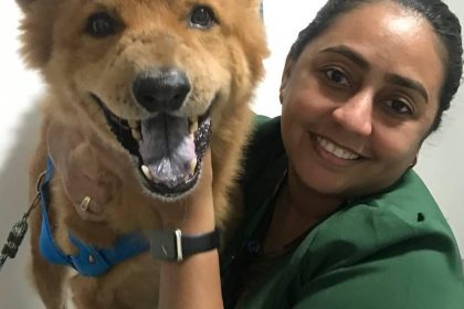 Mulher sorrindo abraçando um cachorro com sinais de câncer.