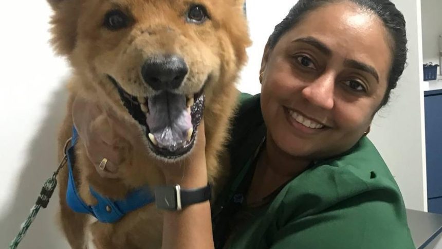 Mulher sorrindo abraçando um cachorro com sinais de câncer.